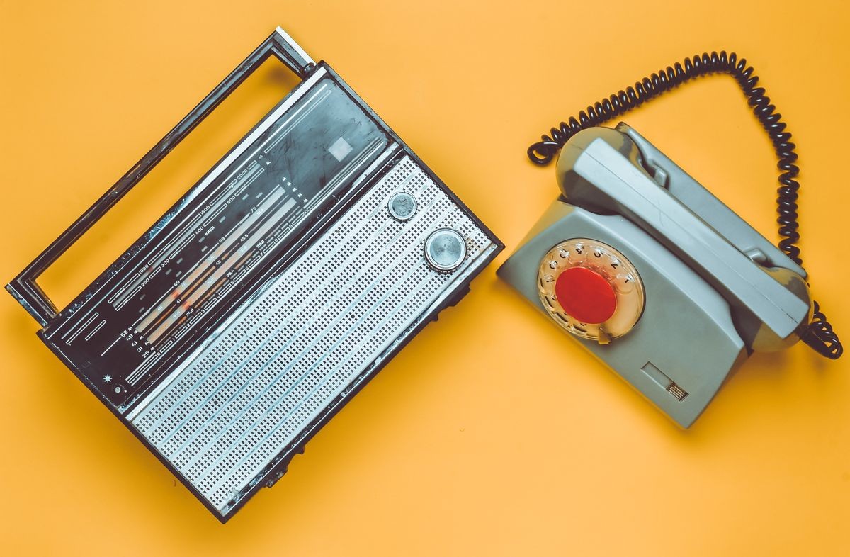 Culture of the 70s. Radio receiver and rotary telephone on yellow background. Retro devices. Top view.